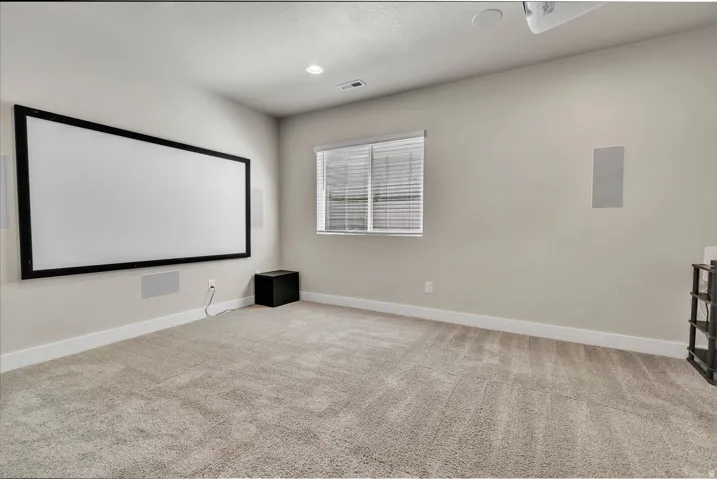 Dedicated media room featuring neutral carpeting, a recessed ceiling with integrated lighting, and a fixed projection screen with black frame