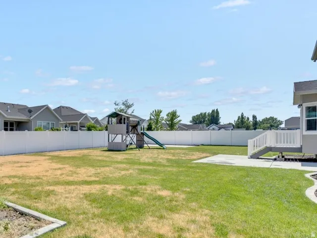 Expansive backyard featuring a mature lawn, concrete edging, and a white vinyl privacy fence