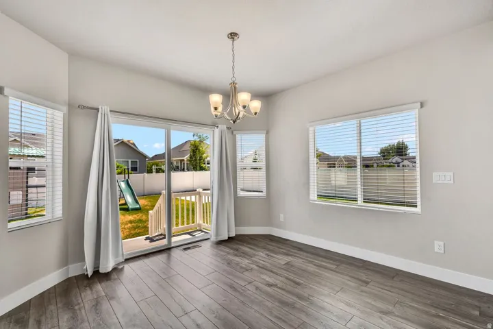 Bright and open dining area featuring gleaming wood-finish flooring, multiple large windows with horizontal blinds, and glass sliding doors opening to a covered deck
