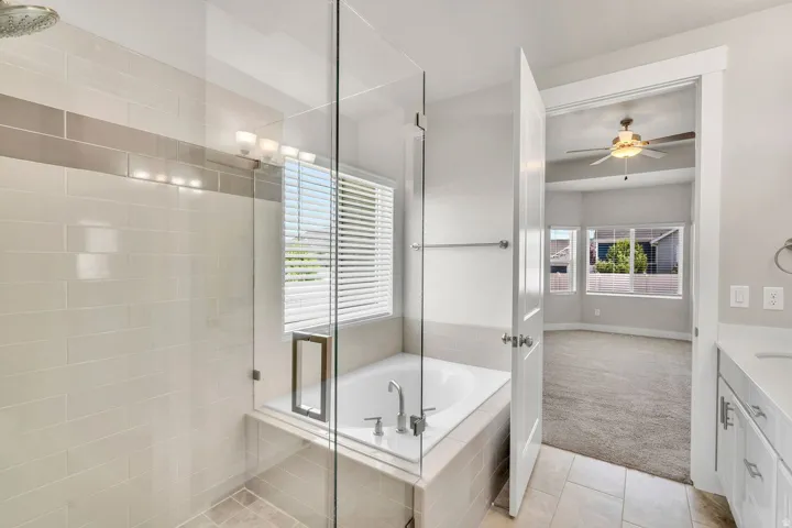 Spa-inspired primary bathroom featuring a frameless glass-enclosed walk-in shower with subway tile surround, a freestanding soaking tub with deck-mounted faucet, dual vanities with white cabinetry, and abundant natural light from operable windows
