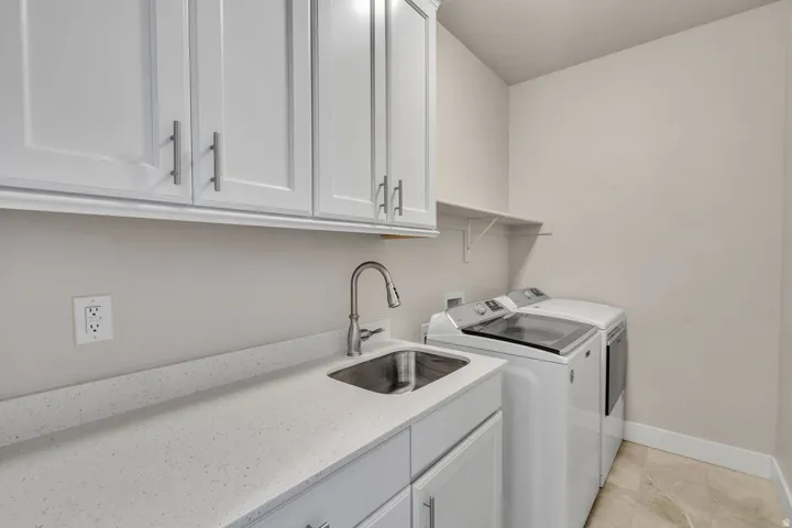 Dedicated laundry room featuring white shaker-style cabinetry, quartz countertops, a stainless steel sink with modern pull-down faucet, and side-by-side washer and dryer hookups