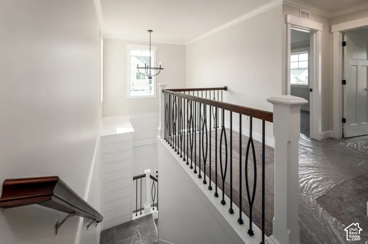 Upper landing featuring a wrought iron and wood handrail, crown molding, and a contemporary chandelier