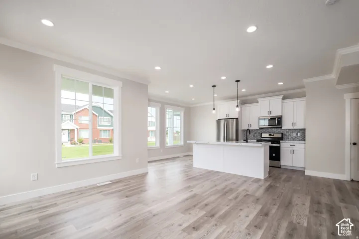 Open-concept living space featuring wood-finish flooring throughout, recessed lighting, and crown molding