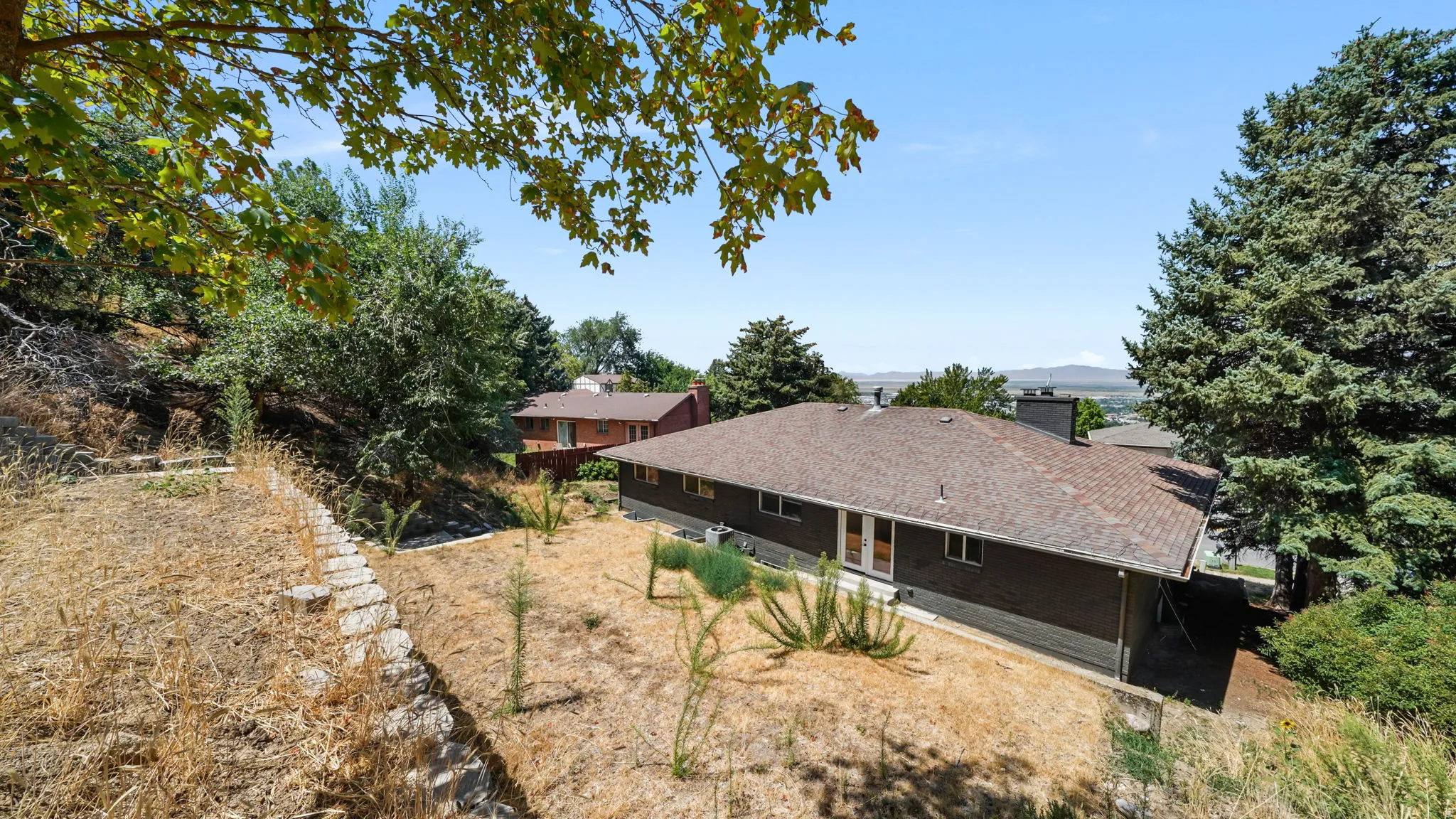 Expansive rural property featuring a single-story residence with a low-pitched roof and dark exterior siding, set on a generous lot with mature trees providing natural shade