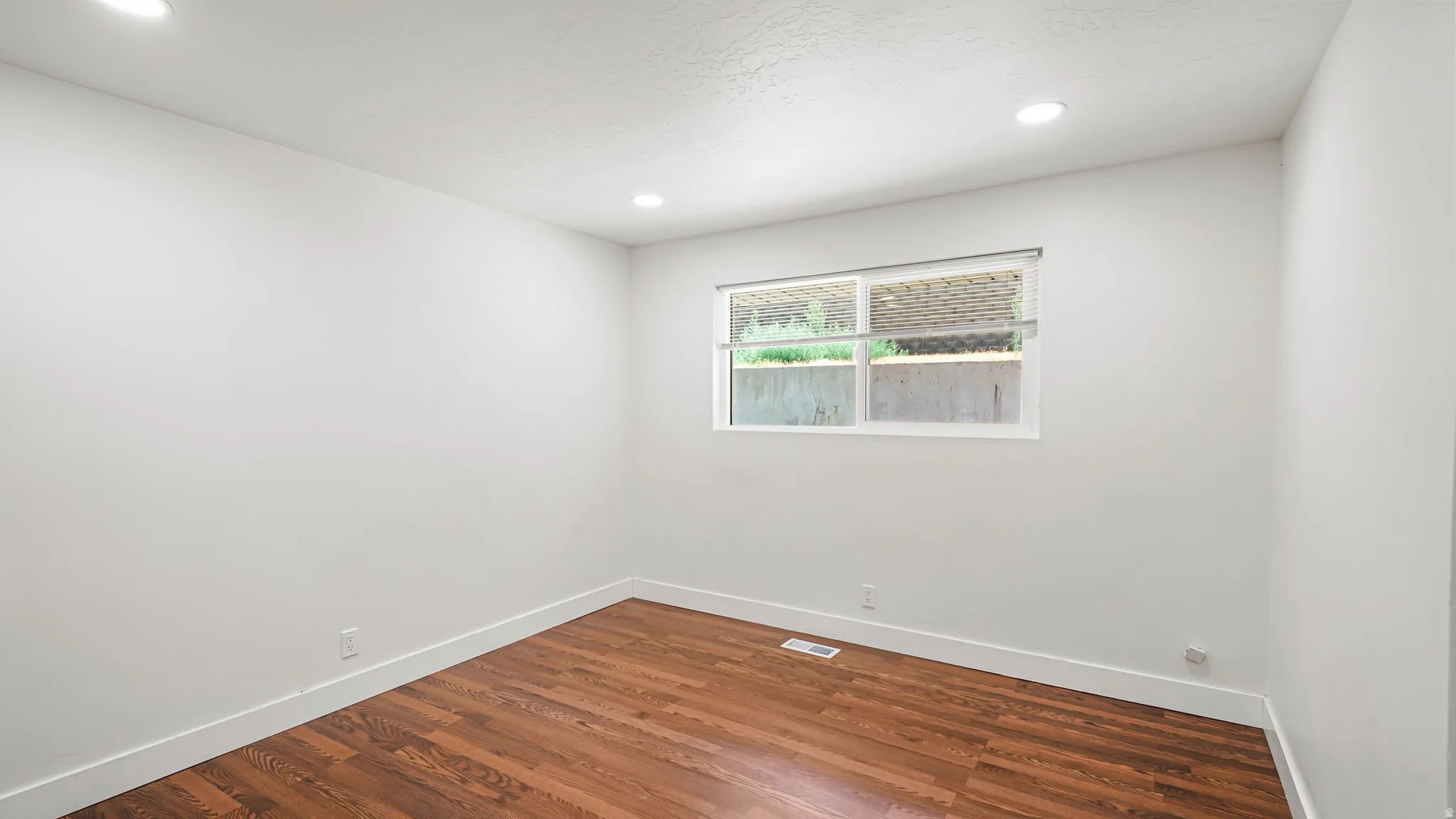 Bright room featuring wood-finish flooring, recessed lighting, white baseboards, and a window with a roller shade