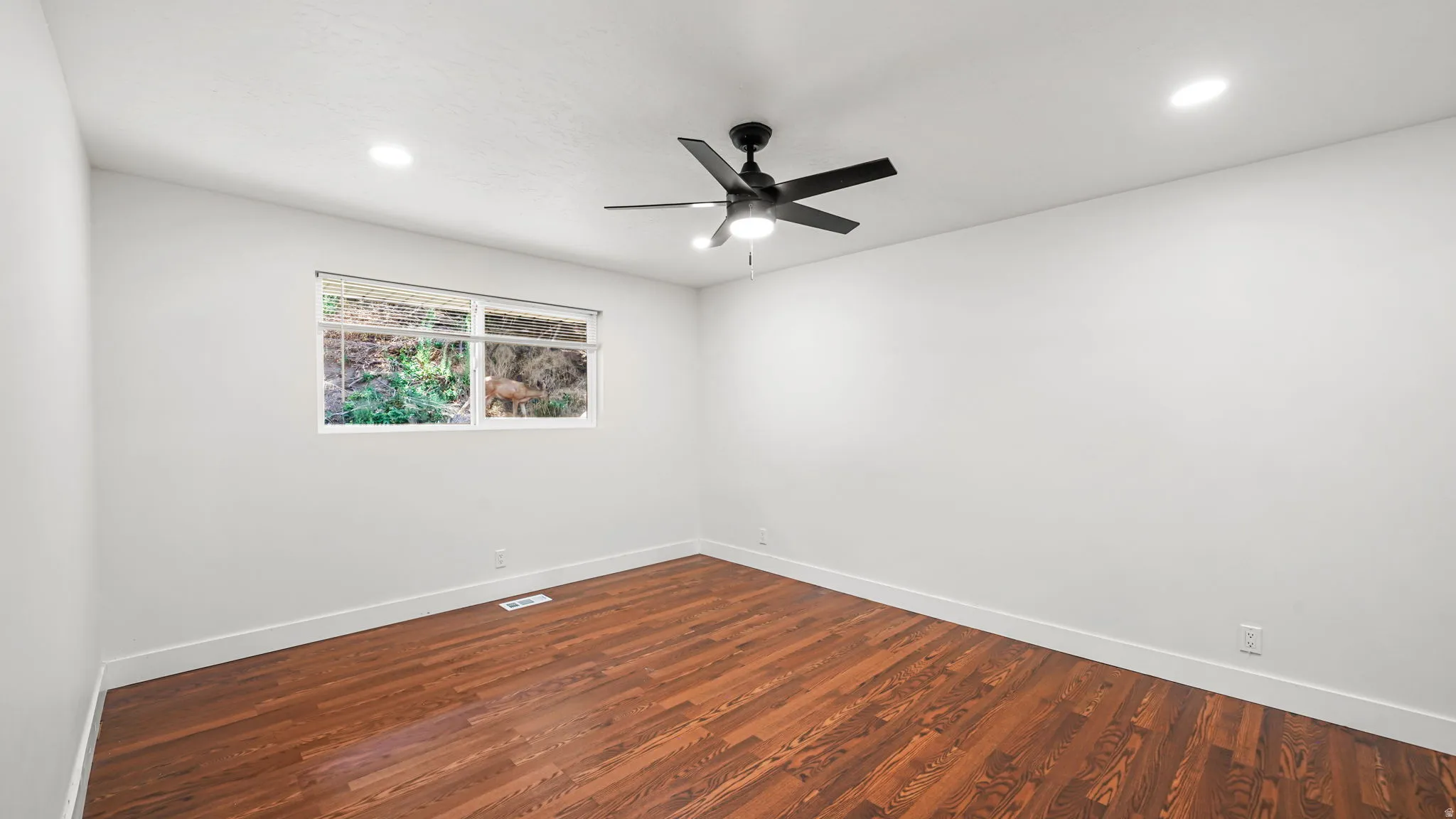 Spacious room showcasing rich wood-finish flooring, clean white walls, and recessed lighting throughout