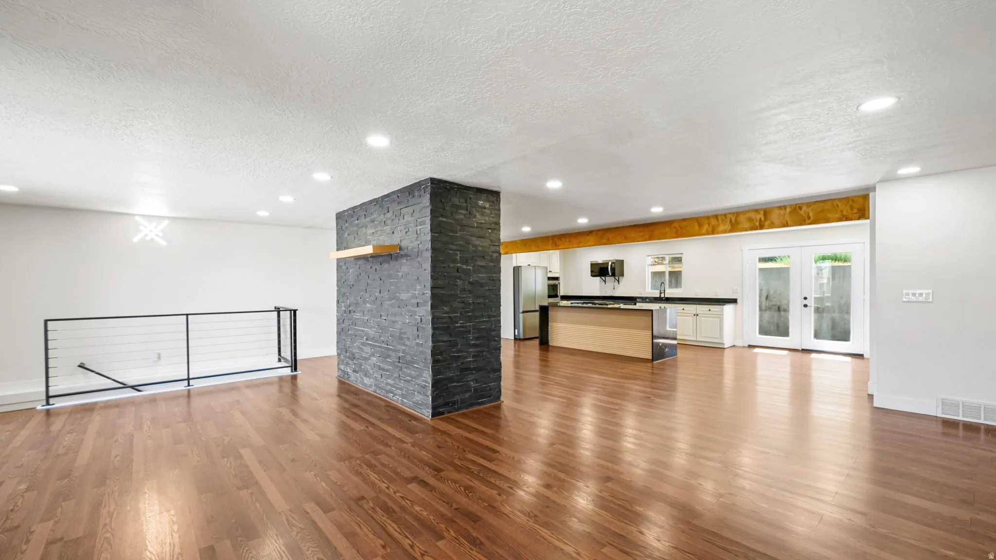 Open-concept living area featuring rich wood-finish flooring, recessed lighting, and a modern black stacked stone accent wall with a wood shelf