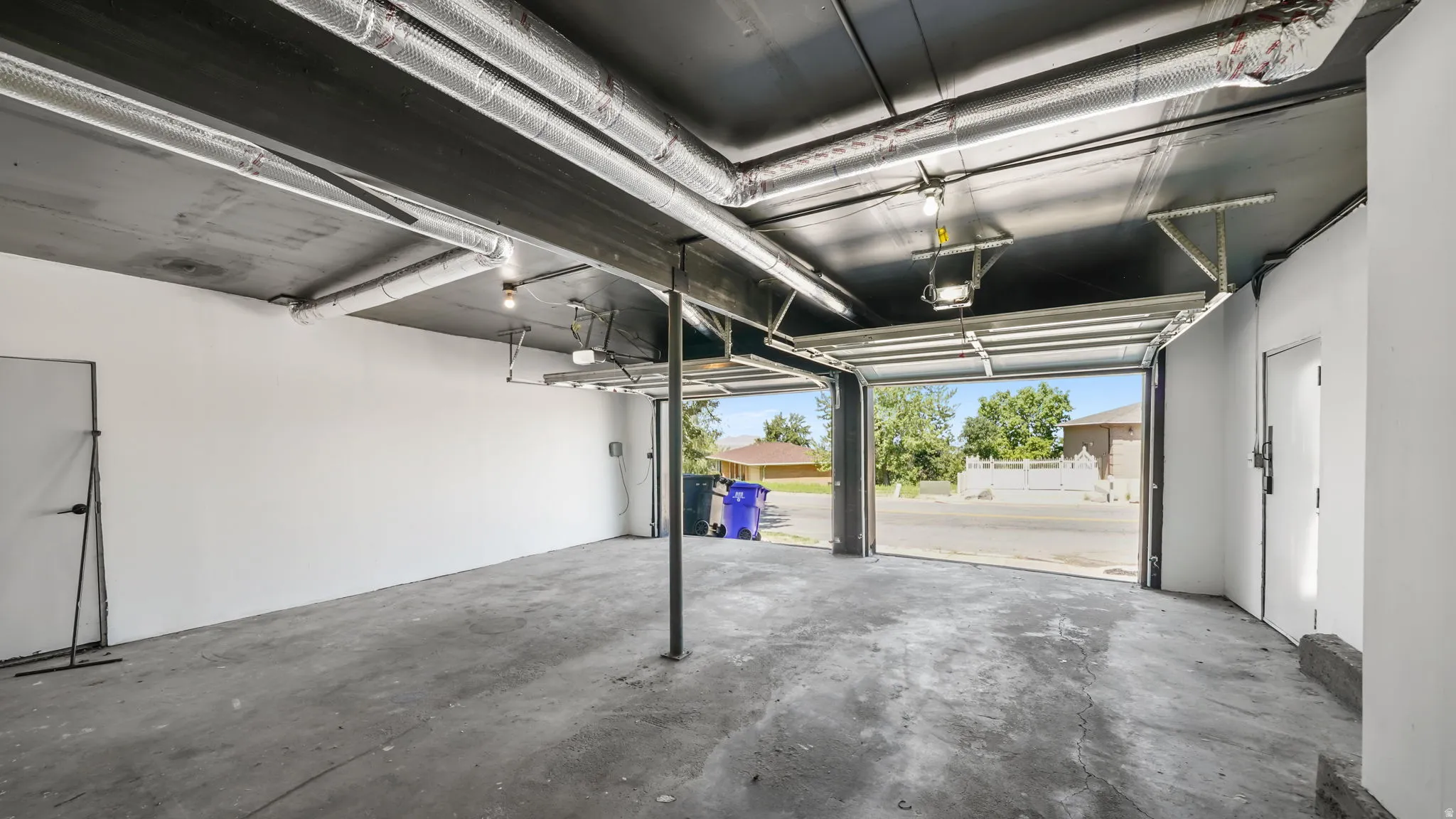 Spacious concrete garage with two overhead doors, exposed ceiling ductwork, and an interior access door