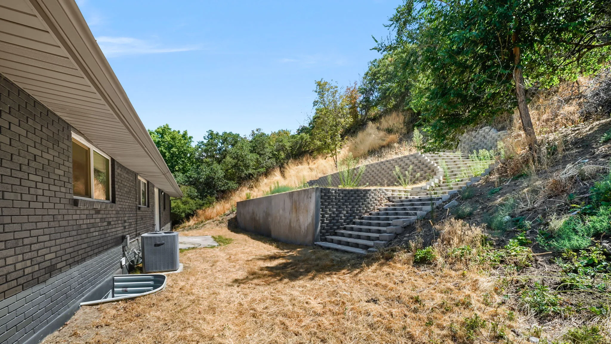 Expansive backyard with sloped terrain, retaining wall, and metal staircase providing access to upper grounds