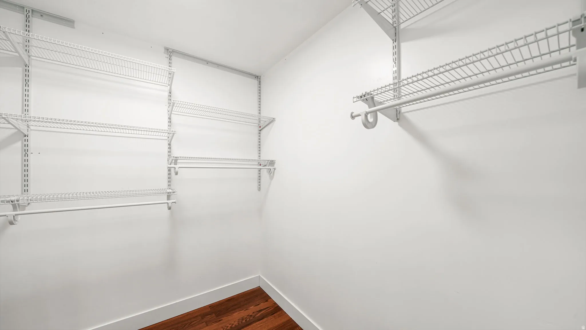Walk-in closet featuring white wire shelving, multiple hanging rods, and wood-finish flooring