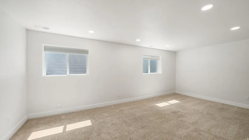 Bright and spacious bedroom featuring recessed ceiling lighting, abundant natural light from dual windows, and neutral carpet flooring throughout