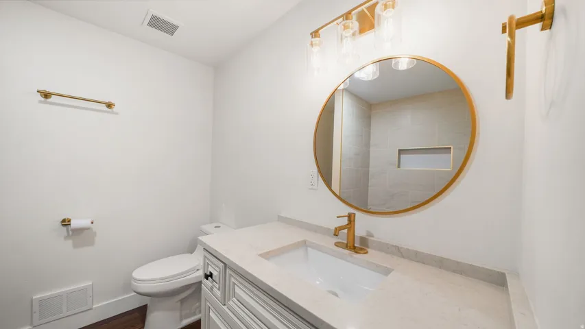 Bathroom featuring a white vanity with recessed paneling, light countertop, undermount sink, and gold-finish hardware