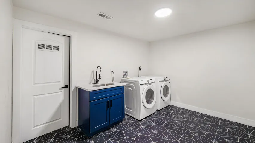 Laundry room featuring patterned geometric floor tiles, a blue vanity with a white countertop and integrated sink, a matte black faucet, and a white paneled door with frosted glass inserts
