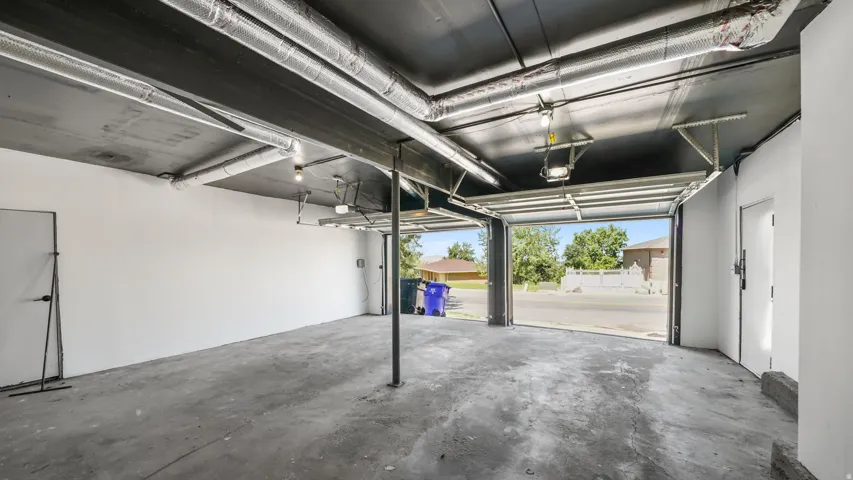 Spacious concrete garage with two overhead doors, exposed ceiling ductwork, and an interior access door