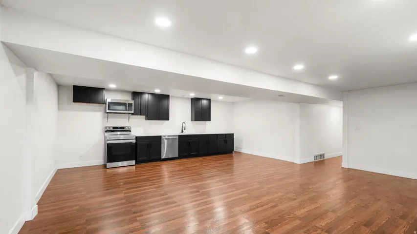 Open-concept area featuring wood-finish flooring, a full kitchen with dark cabinetry, stainless steel appliances, and recessed lighting