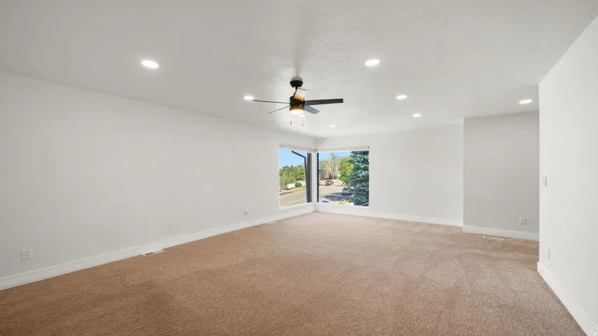 Spacious room featuring neutral carpeting, a corner window offering exterior views, recessed lighting, and a ceiling fan