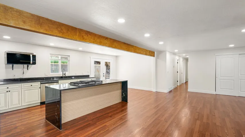 Open-concept kitchen and living area featuring a large center island with cooktop, recessed lighting, wood-finish flooring, and a prominent exposed ceiling beam