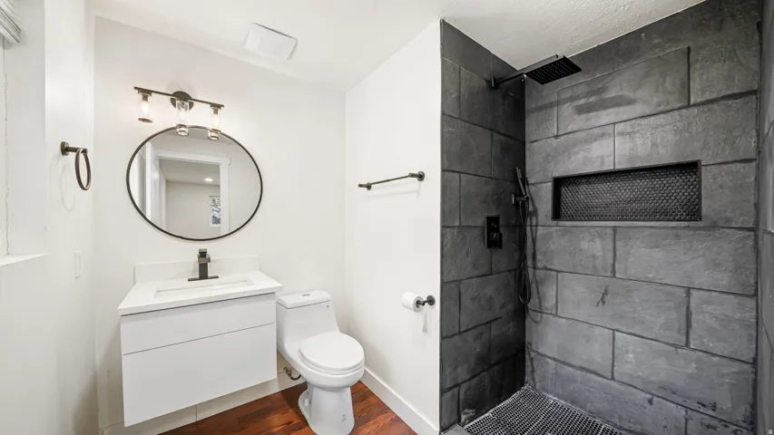 Modern primary bathroom featuring a floating vanity with rectangular vessel sink, matte black hardware, and round mirror with integrated lighting