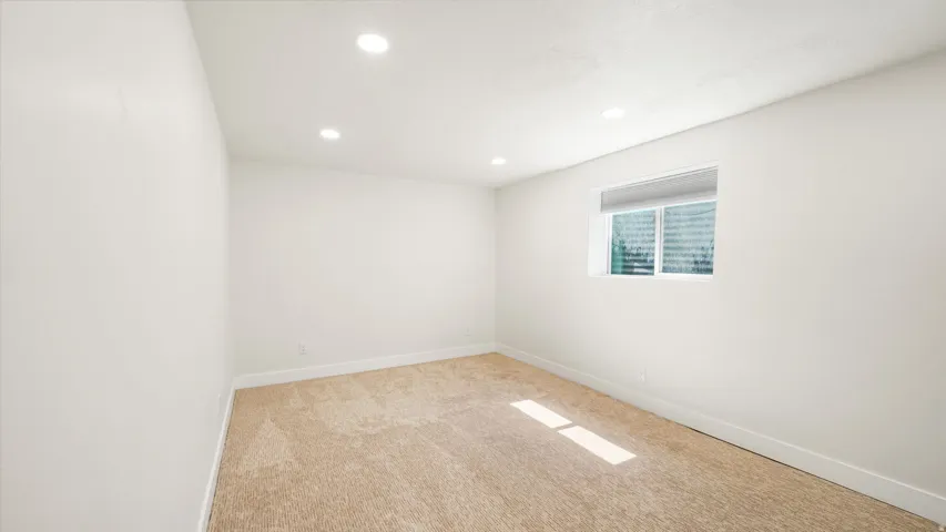 Bright room featuring recessed lighting, a horizontal window with blinds, light-colored carpeting, white walls, and white baseboards