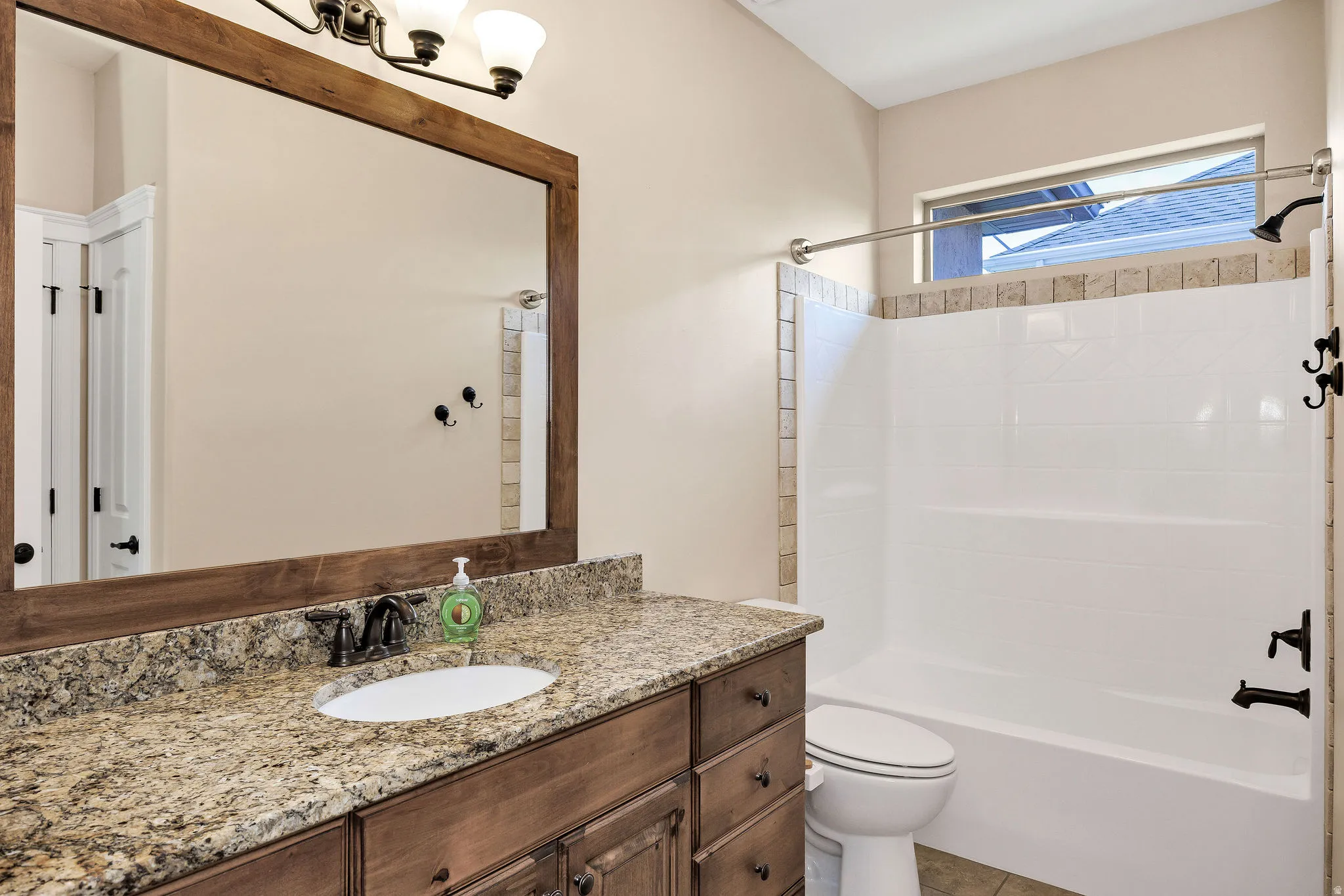 Bathroom featuring a wood-framed mirror, granite countertop vanity with an undermount sink, dark bronze fixtures, and a shower-tub combination with tile surround accents