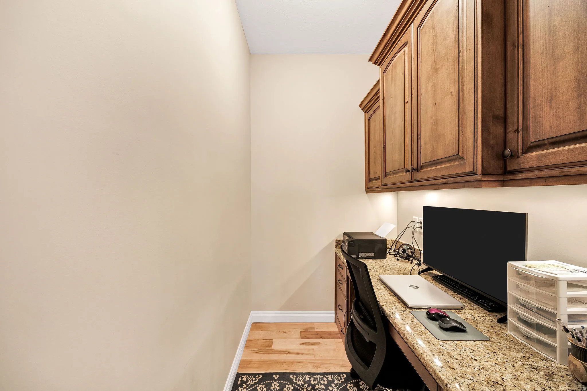 Dedicated workspace featuring wood-finish flooring, built-in cabinetry with under-cabinet lighting, a granite countertop, and a built-in desk