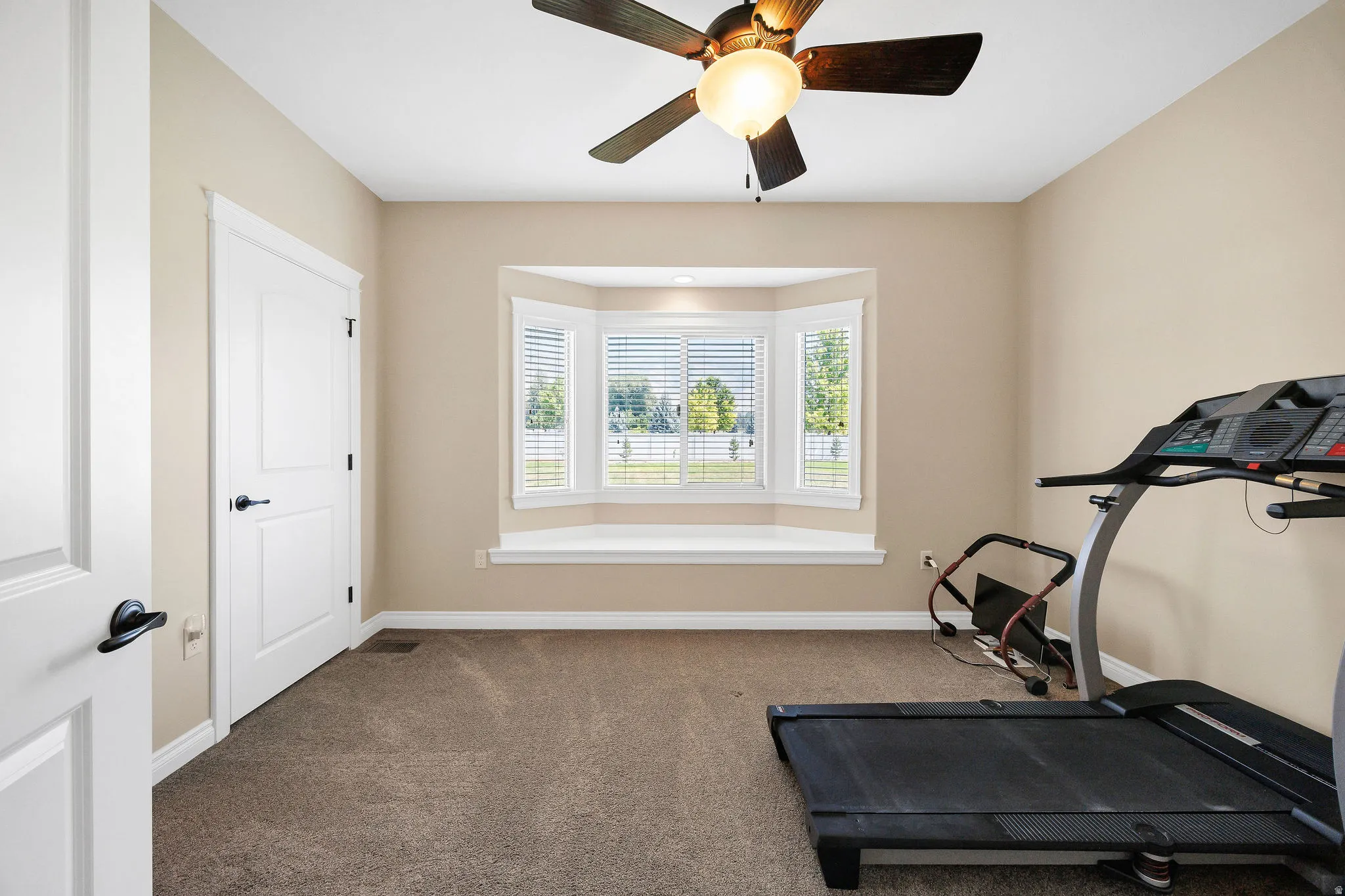 Carpeted room featuring a ceiling fan with integrated lighting, a multi-pane bay window with plantation shutters, and a window seat