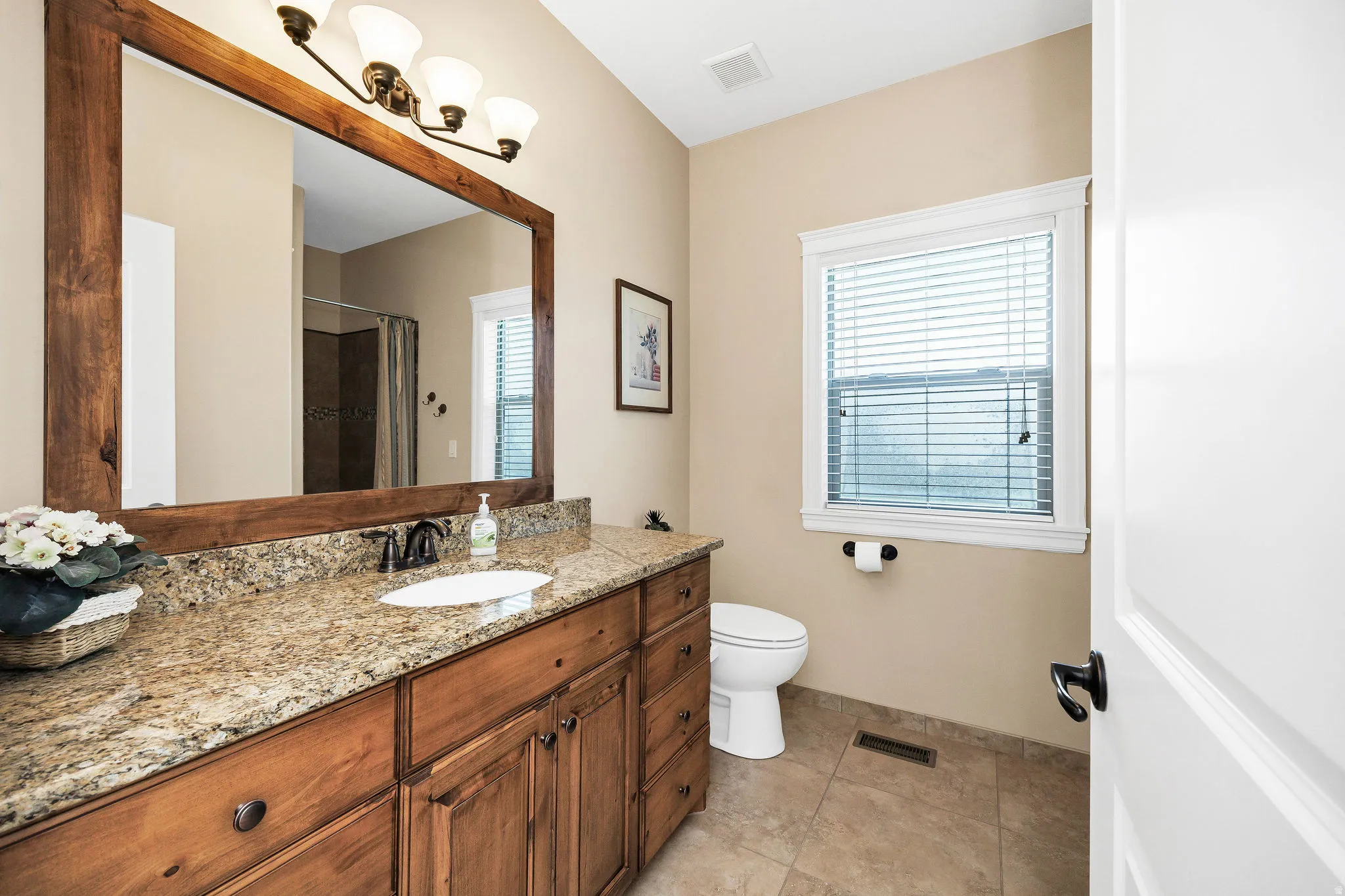 Bathroom featuring a wood-framed mirror, four-light vanity fixture, an elongated vanity with wood cabinetry, a built-in sink, and a speckled countertop