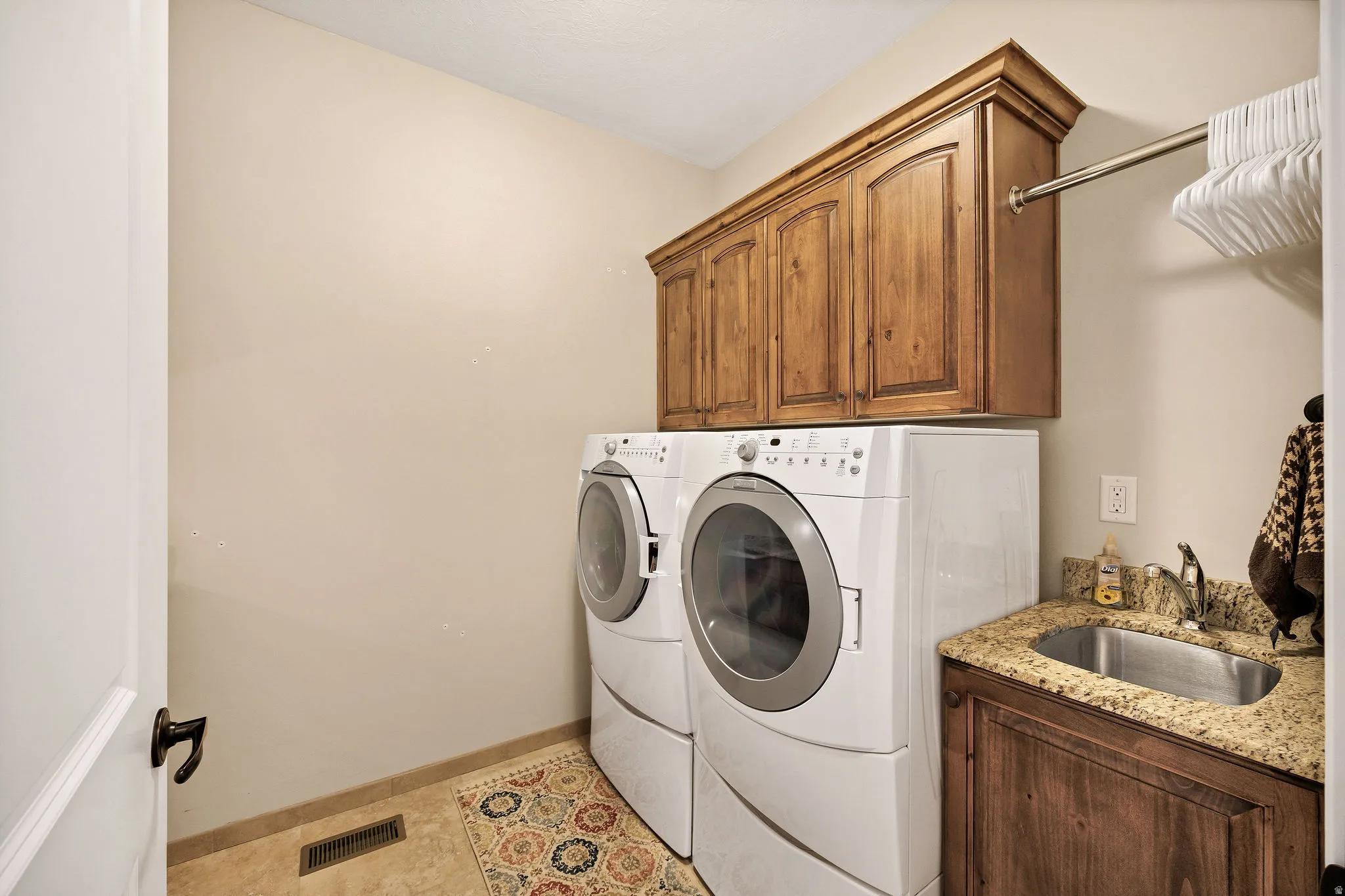 Dedicated laundry room featuring side-by-side front-load washer and dryer with white finish, custom wood cabinetry with crown molding, granite-style countertop with integrated sink, wood-finish flooring, and abundant storage