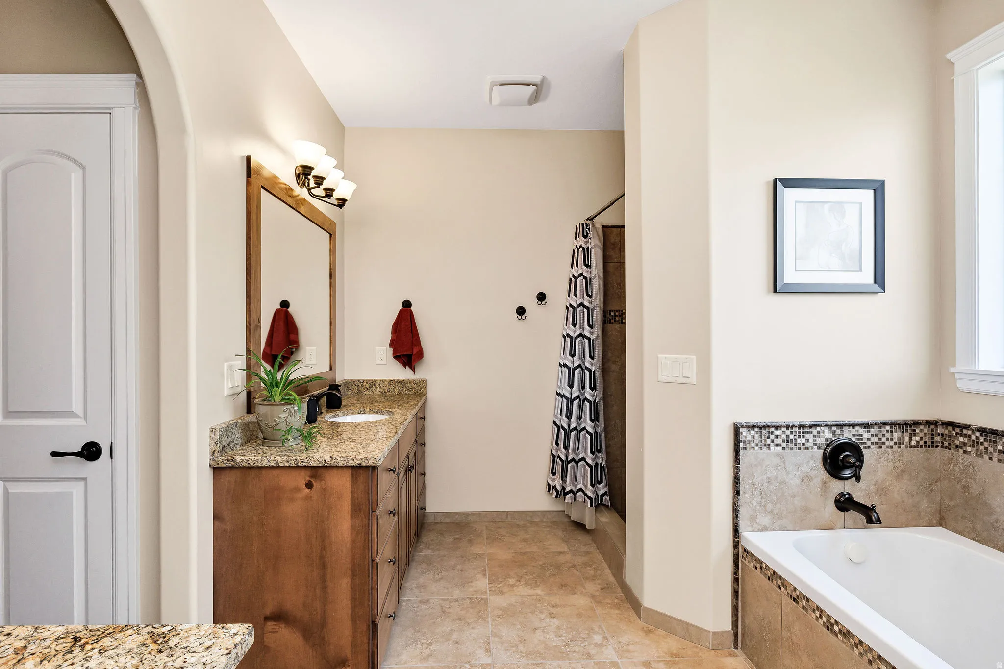 Spa-inspired master bath featuring dual vanities with granite countertops, wood-finish cabinetry, and a large soaking tub with tile surround