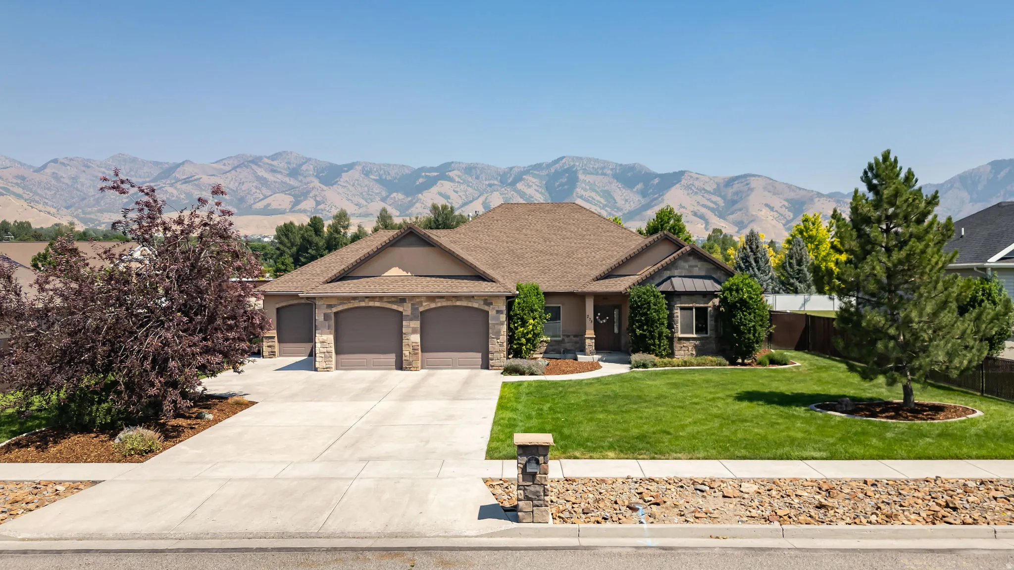 Ranch-style residence featuring a stone and stucco exterior, an attached three-car garage, and a concrete driveway