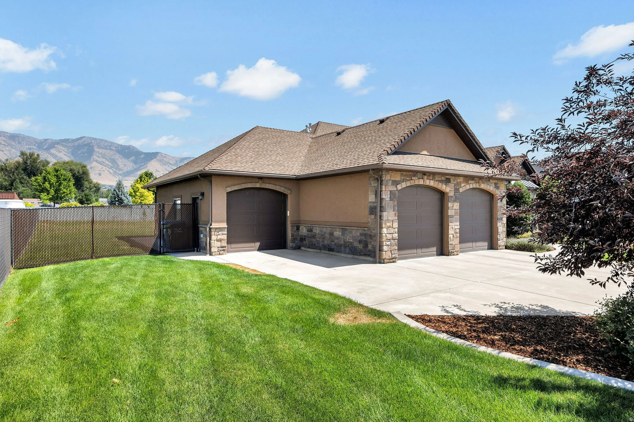 Stucco and stone facade featuring a two-car garage with arched doors, a paved driveway, a manicured lawn, and a side access gate