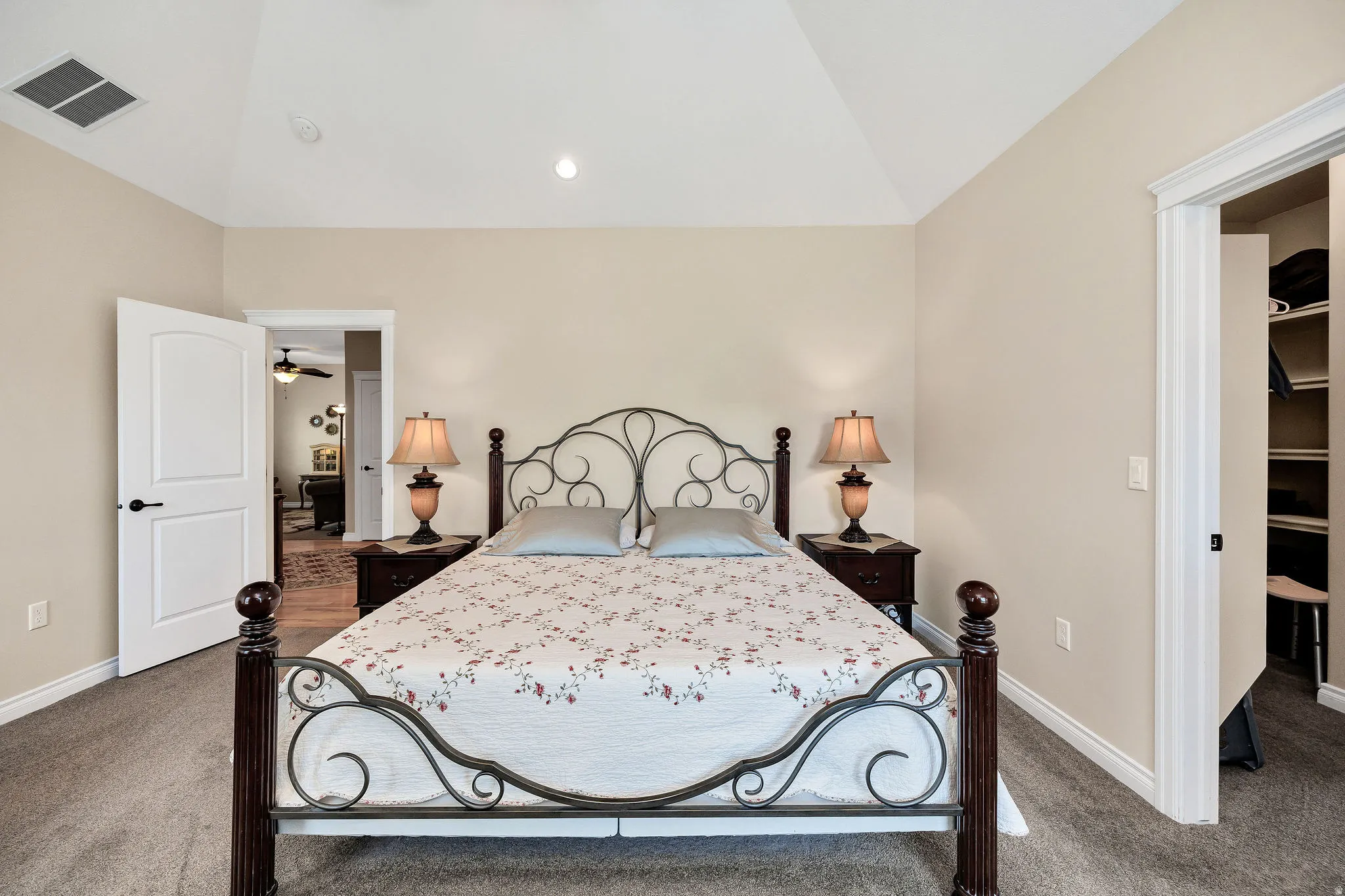 Bedroom featuring vaulted ceilings, neutral wall tones, carpet flooring, and an open doorway revealing a closet with built-in shelving