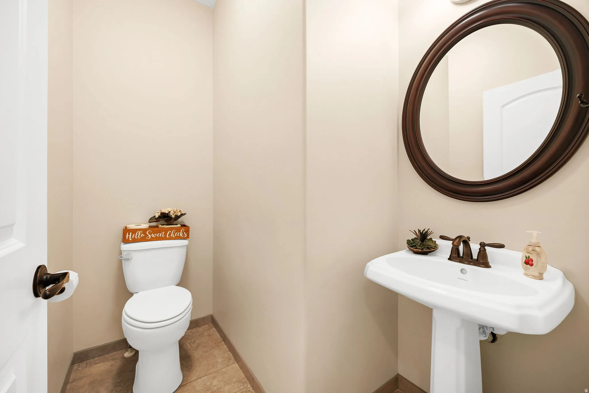Powder room featuring a pedestal sink with bronze hardware, an oval framed mirror, and tile flooring