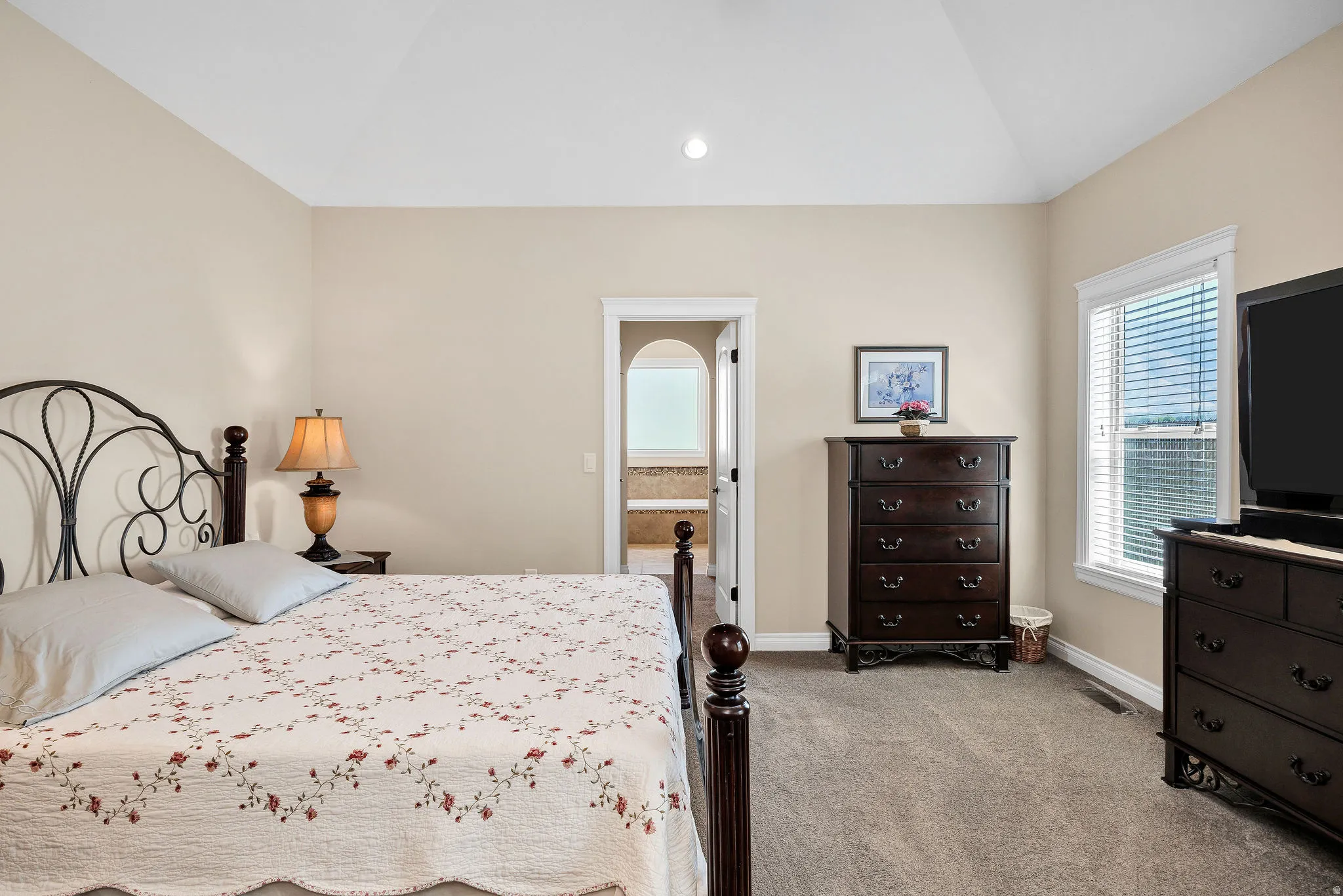 Spacious bedroom featuring an ornamental metal bed frame, warm neutral wall finishes, recessed ceiling lighting, and carpet flooring