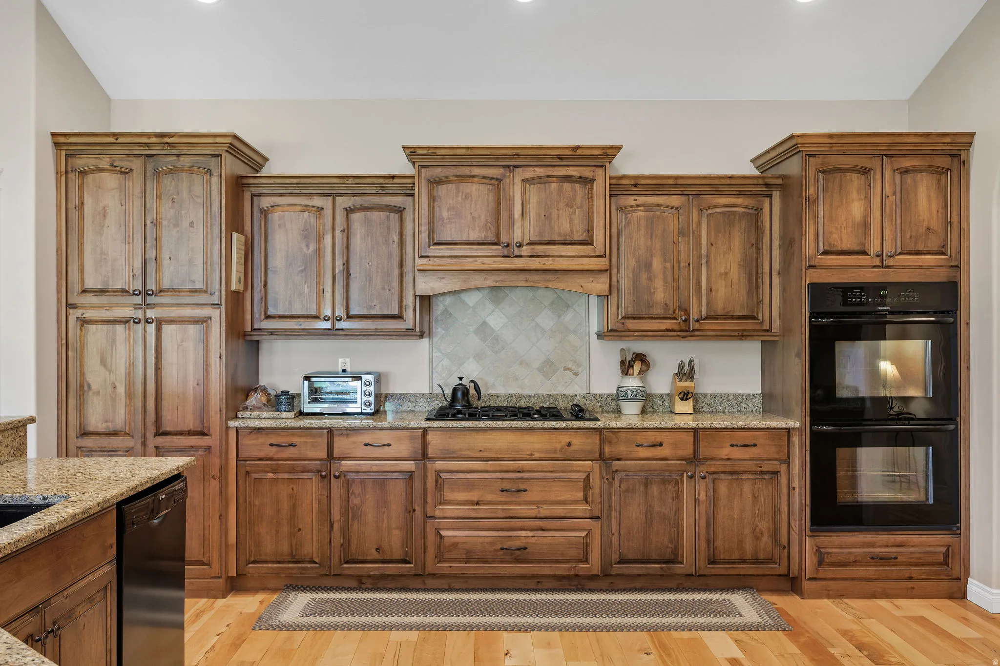 Custom wood cabinetry with upper and lower storage, granite countertops, and a tiled backsplash