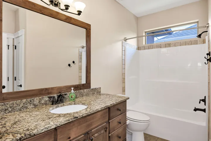 Bathroom featuring a wood-framed mirror, granite countertop vanity with an undermount sink, dark bronze fixtures, and a shower-tub combination with tile surround accents