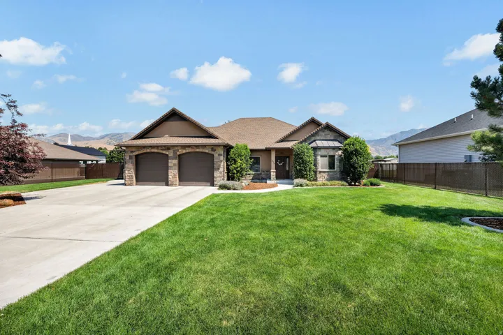 Single-story residence featuring a stone and stucco exterior, a two-car garage with arched entrances, a wide concrete driveway, and a front lawn with mature landscaping