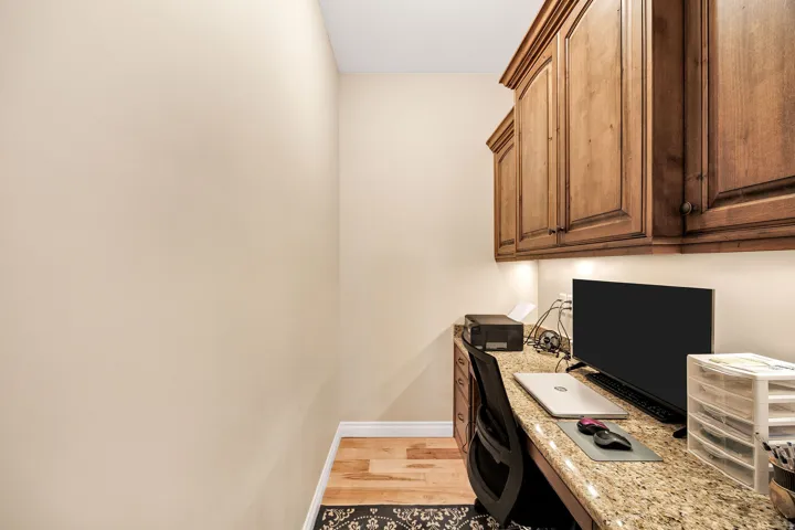 Dedicated workspace featuring wood-finish flooring, built-in cabinetry with under-cabinet lighting, a granite countertop, and a built-in desk