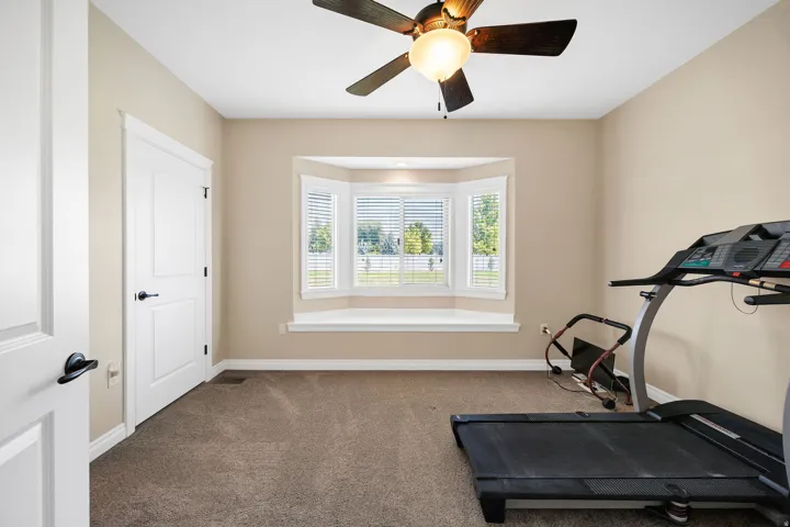 Carpeted room featuring a ceiling fan with integrated lighting, a multi-pane bay window with plantation shutters, and a window seat