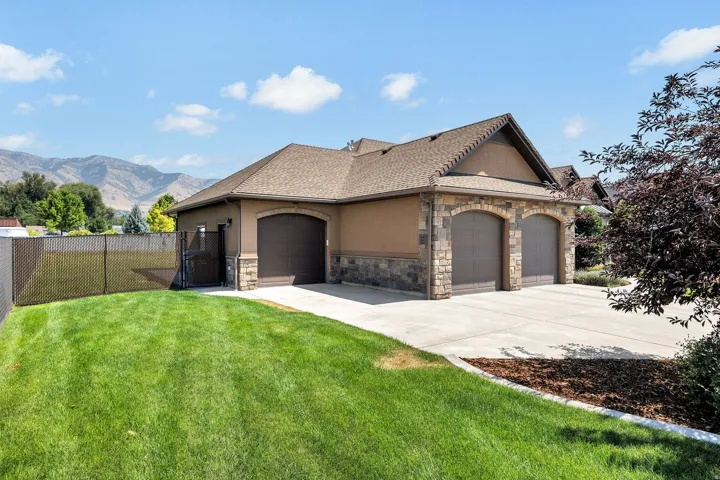 Stucco and stone facade featuring a two-car garage with arched doors, a paved driveway, a manicured lawn, and a side access gate