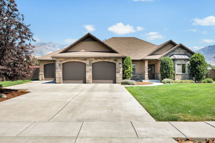 Single-story residence featuring a stone and stucco exterior, an extended driveway, a three-car garage with arched entries, and a bay window