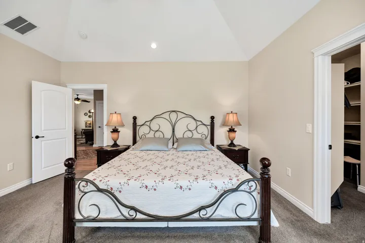 Bedroom featuring vaulted ceilings, neutral wall tones, carpet flooring, and an open doorway revealing a closet with built-in shelving