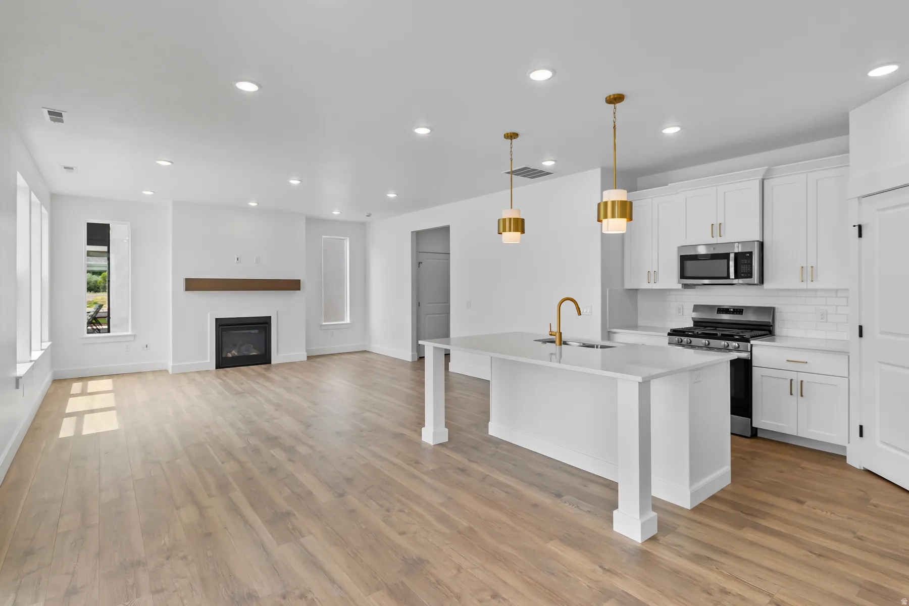 Open-concept kitchen and living area featuring white cabinetry, stainless steel appliances, and a large island with waterfall-edge countertop