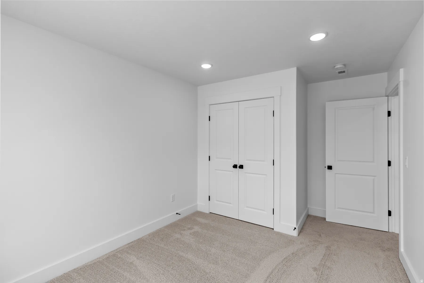 Spacious secondary bedroom featuring pristine white panel doors, recessed ceiling lighting, and neutral carpet flooring throughout