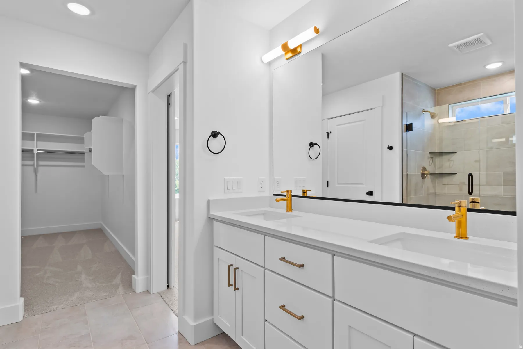 Spa-inspired primary bathroom featuring a dual-sink vanity with white cabinetry, brushed brass hardware, and a quartz countertop