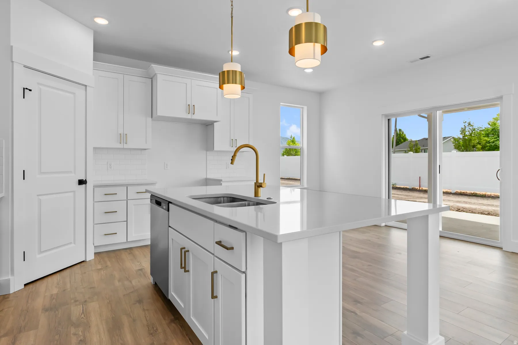 Modern kitchen featuring white cabinetry, a large waterfall-edge island with integrated storage and seating, stainless steel cooktop, brass pendant lighting, and brushed brass faucet