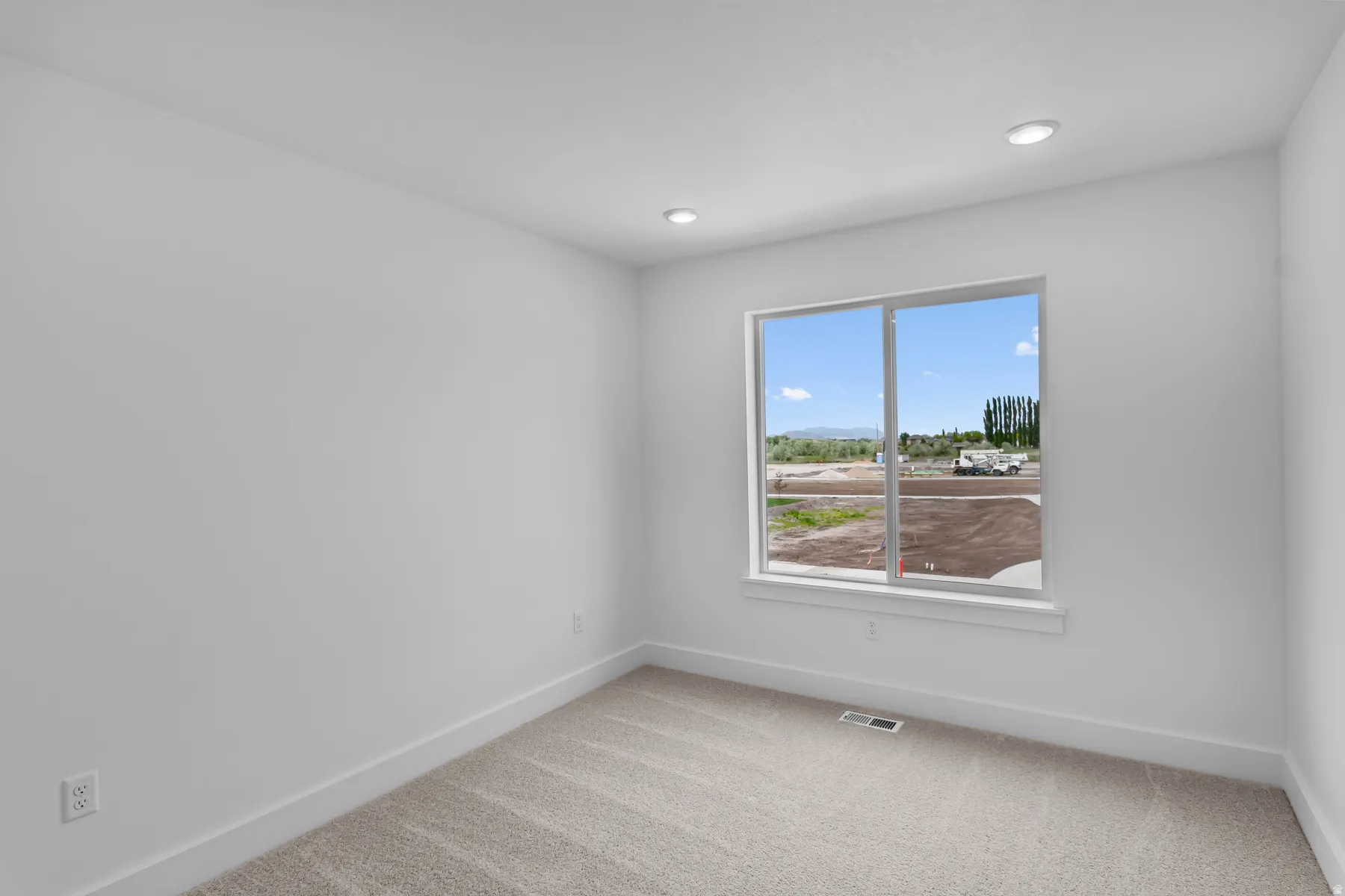 Bright bedroom featuring abundant natural light from a large double-hung window, neutral wall finishes, recessed ceiling lighting, and wood-finish flooring throughout