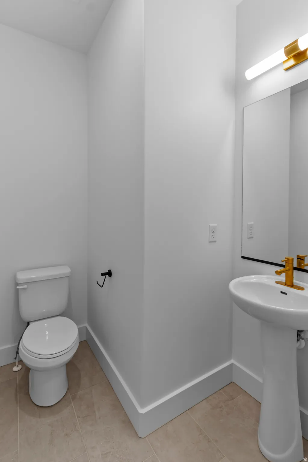 Bright, functional bathroom featuring a ceramic pedestal sink with brass-finished fixtures, white subway tile walls, recessed lighting, and a separate water closet with elongated bowl toilet