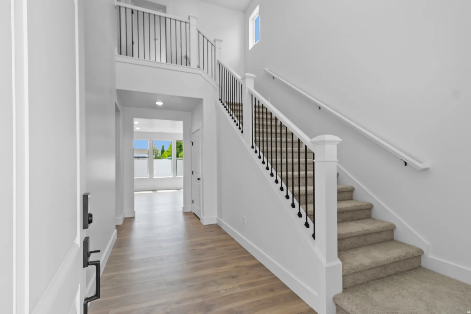 Bright foyer with wood-finish flooring and clean white walls, anchored by a curved staircase featuring white newel posts and black metal balusters