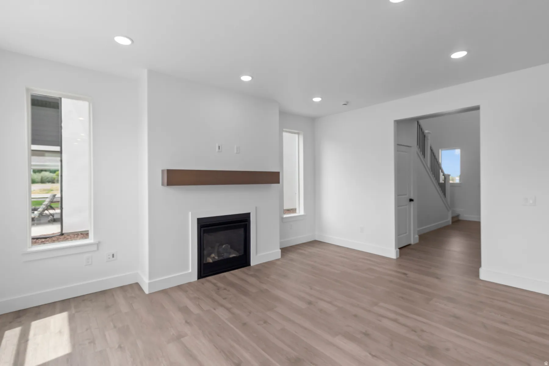 Open-concept living space featuring wood-finish flooring, recessed lighting, and a modern fireplace with a wood mantle